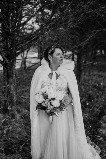 A solo portrait of Lexi in her wedding cape, holding her bouquet and staring off into the distance.