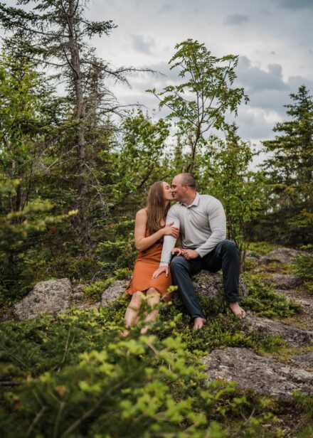 A couple kisses sitting on a rock in the woods on Palisade Head