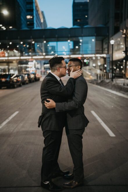The grooms lean in for a kiss under the city lights in the middle of the street.