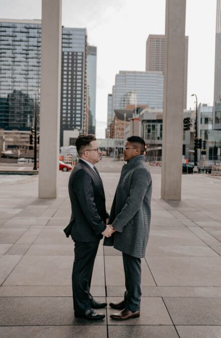Zane and David face each other holding hands, Minneapolis skyscrapers in the background.