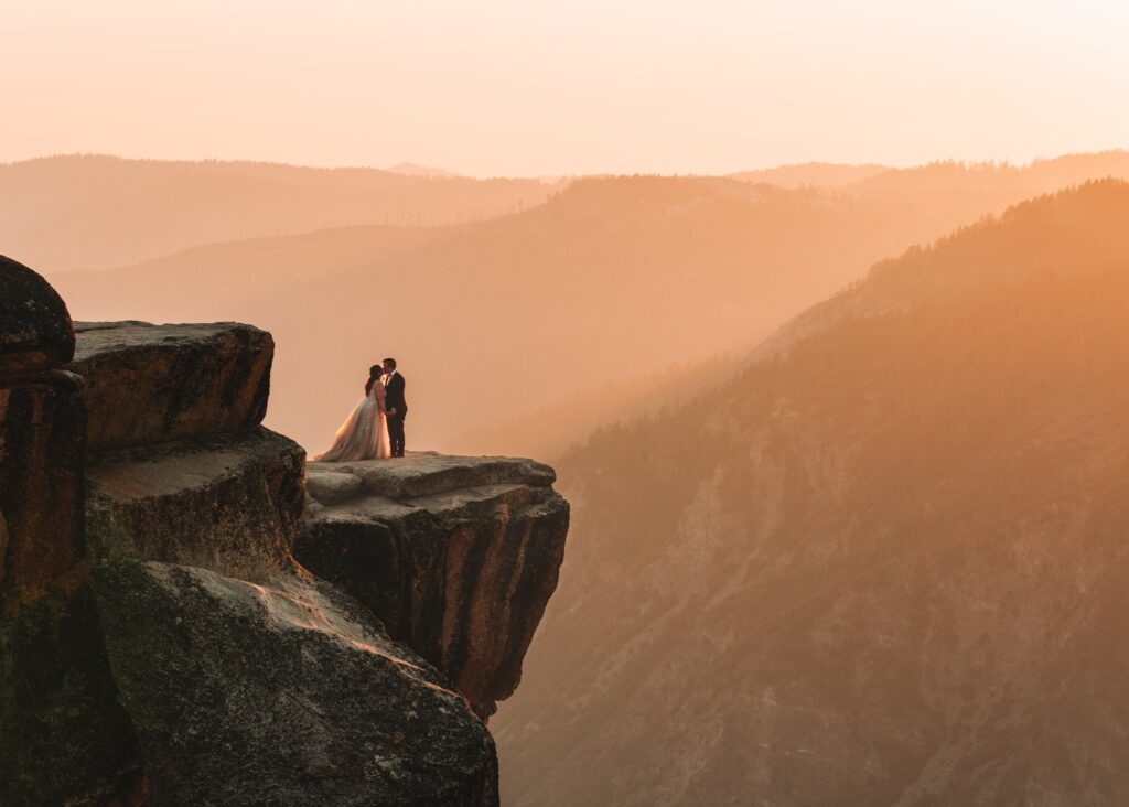 A couple standing on a cliff during an orange sunset after their elopement in Yosemite National Park