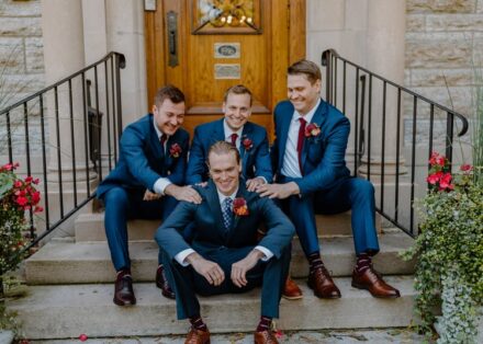 Tom and his groomsmen sit on the steps, the groomsmen giving him pats of encouragement.