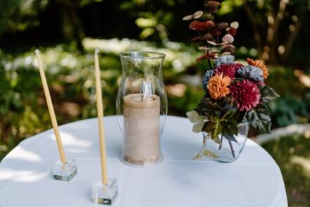 A close up of the unity candle on a table next to a vase of wooden flowers.
