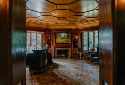 A wide angle shot of the bar with wood paneled ceilings and an ornate fireplace.