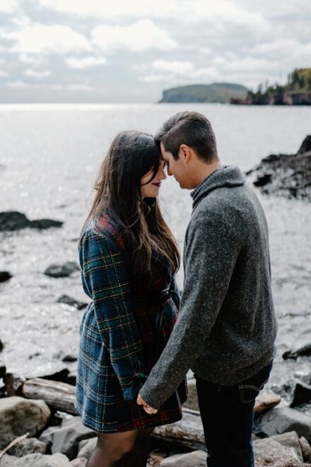Alison and Sebastein hold hands and press their foreheads together in front of Lake Superior.