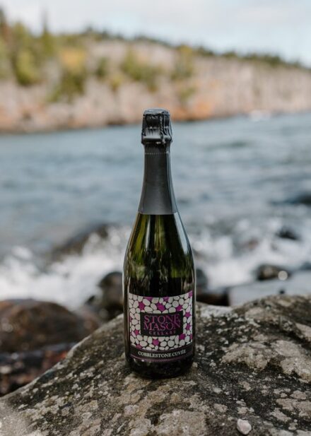 A bottle of champagne sitting on a rock in front of Lake Superior.