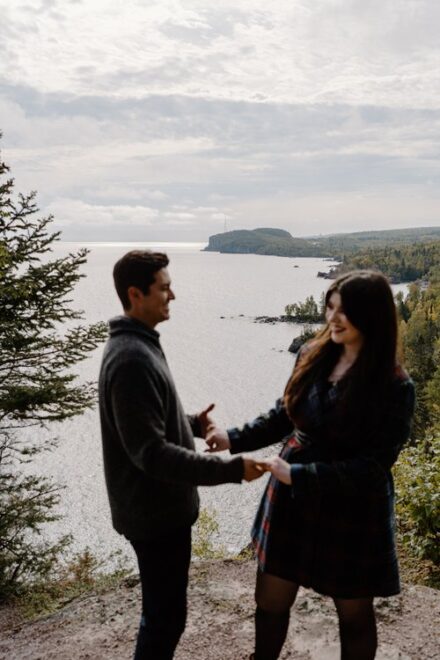 Alison and Sebastein hold hands and laugh on cliff at Shovel Point in Tettegouche State Park.