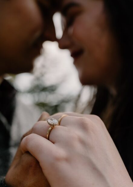 A close up of Alison's engagement ring, with Alison and Sebastein's faces out of focus on the background.