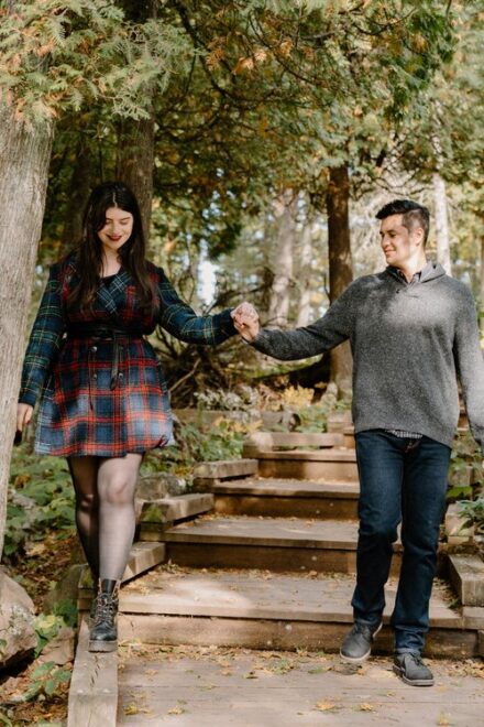 Alison walks along the edge of a wooden trail walkway as Sebastein holds her hand.