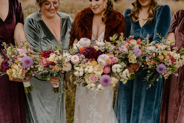Bridesmaids in mismatched velvet dresses and the bride holding out their whimsical wildflower bouquets.