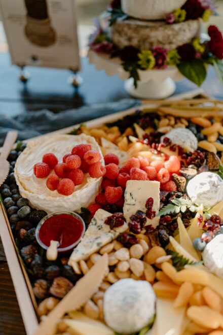 A huge charcuterie board sitting in the sunlight with raspberries, nuts, and lots of cheeses!