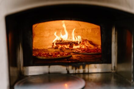 A close up of the wood-fired pizza oven with pizzas baking inside.