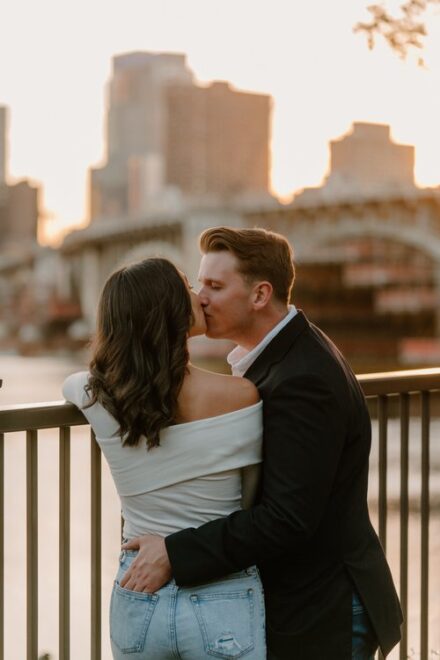 Ashley & Ehren kissing in front of the city skyline during the orange glow of sunset.