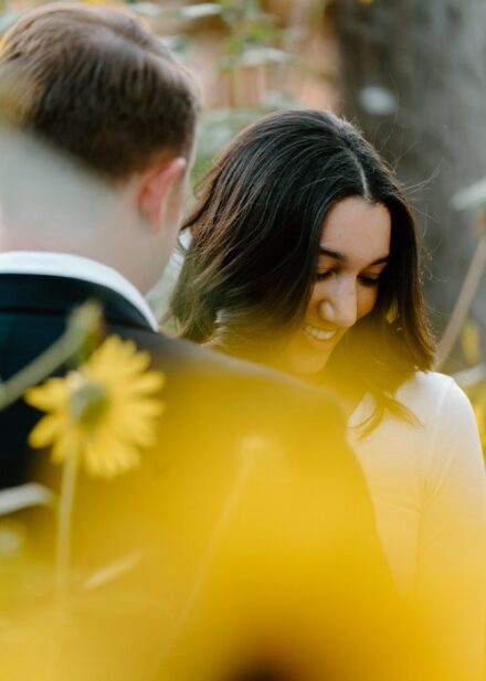 Ashley looks down at her shoulder in front of Ehren, with sunflowers in front of the lens.