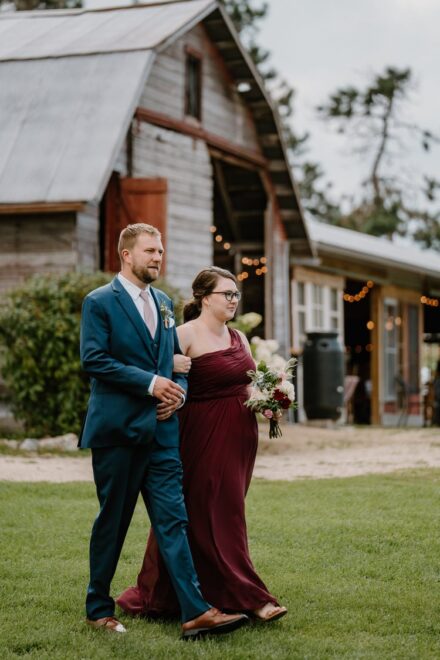 A bridesmaid in a wine red dress walking down the aisle with a groomsman.