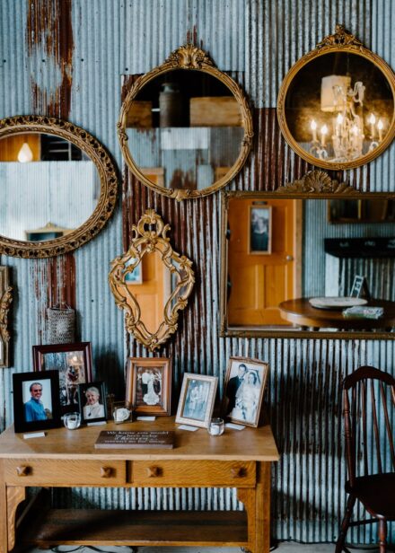 A rustic corrugated metal wall covered in antique mirrors with ornate gold frames.