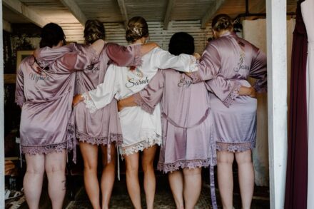 Sarah and her bridesmaids facing away from the camera with their arms wrapped around each other in silk robes.