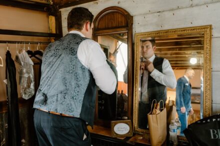 A reflection of Jake putting on his tie in a mirror in the groom's suite.