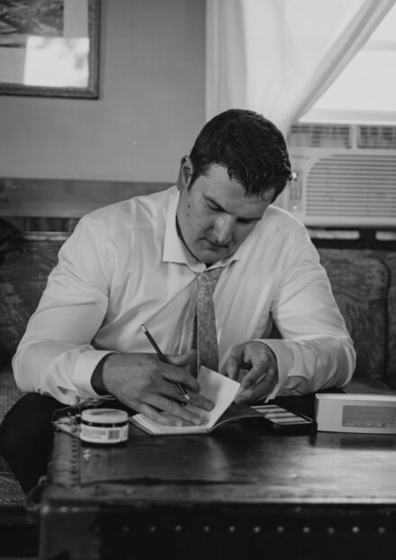 Jake writing his wedding vows on a coffee table in the groom's suite.