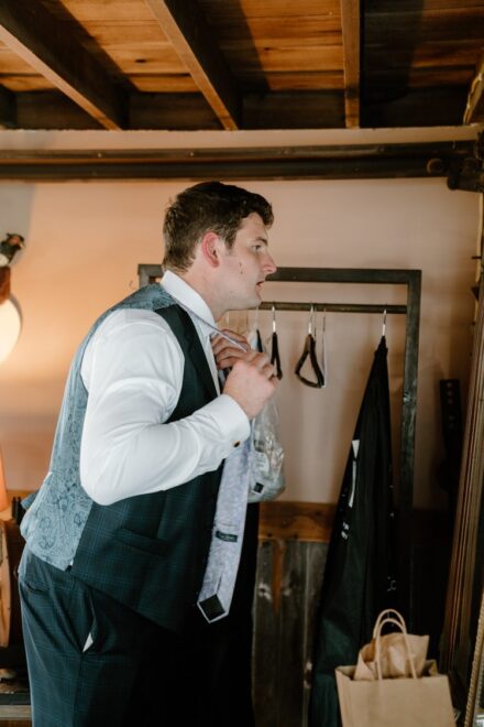 Jake putting on his grey tie in a mirror in the groom's suite.