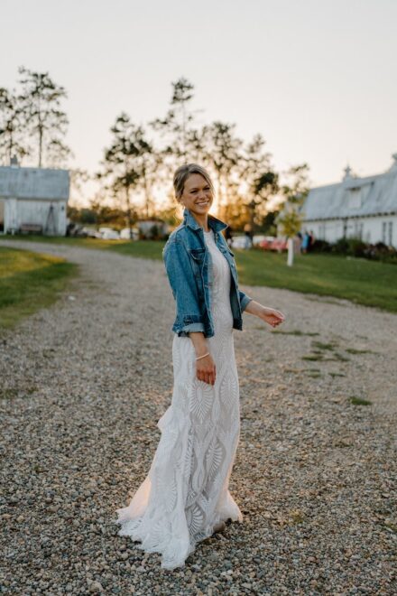 Sarah spins toward the camera in her wedding dress and denim jacket at sunset.