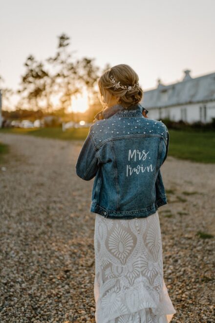 Sarah faces away from the camera and pops the collar of her denim jacket, with the glow of the sunset over her shoulder.