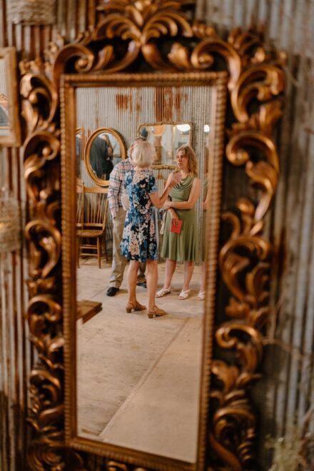 Wedding guests talk to each other in the reflection of an ornate gold mirror.
