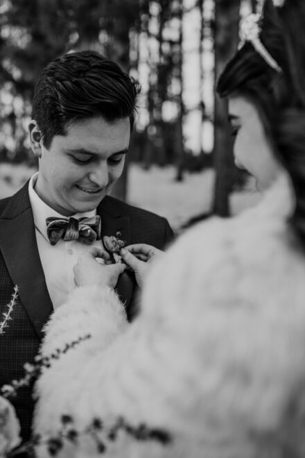 A black and white image of a bride pinning a boutonniere on the groom.