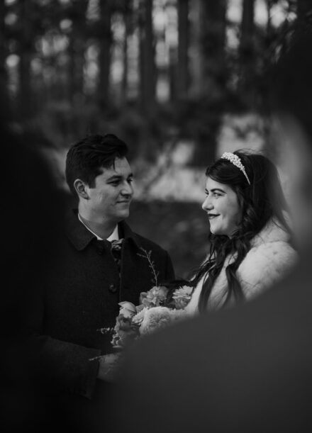 A black and white photo of a wedding couple taken over the shoulder of the bride's parents.
