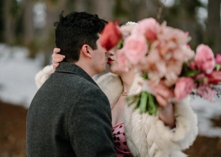 A couple's first kiss after getting married covered by the bride's bright pink bouquet.
