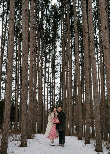 A couple standing underneath tall pines trees after their elopement in Stillwater, Minnesota.