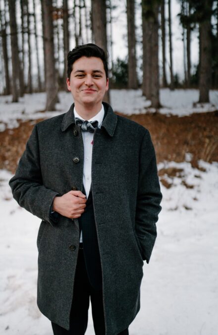A groom holding his jacket and smiling at the camera on his elopement day in Stillwater, Minnesota.