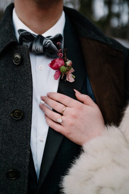 A close up of a bride's hand on her husband's chest underneath his pink boutonniere.