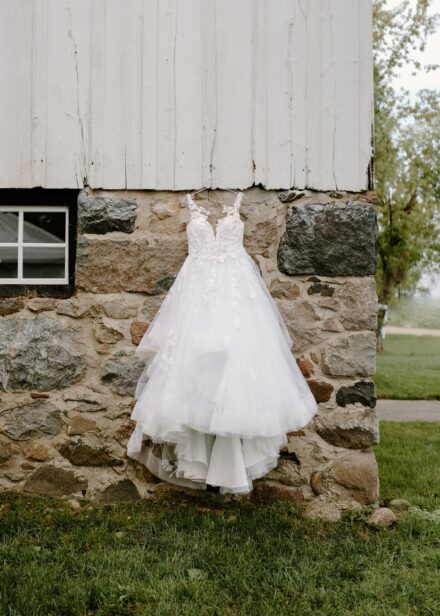 A white tulle ball gown hanging on the side of a stone barn.