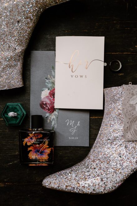 Rhinestone covered boots, perfume, wedding invitations, and ring box flat lay.