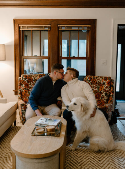 Marko and Andy kiss while sitting on vintage floral arm chairs, with their dog Albert sitting in front of them.
