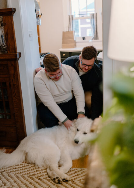 Andy and Marko crouch down on the floor to give their dog, Albert, some pets.