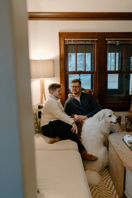 Andy and Marko sit on a white sofa and vintage floral chair, framed by a walkway in front of the camera.