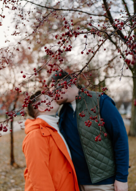 Andy and Marko kiss, their faces covered by red berries on a tree.