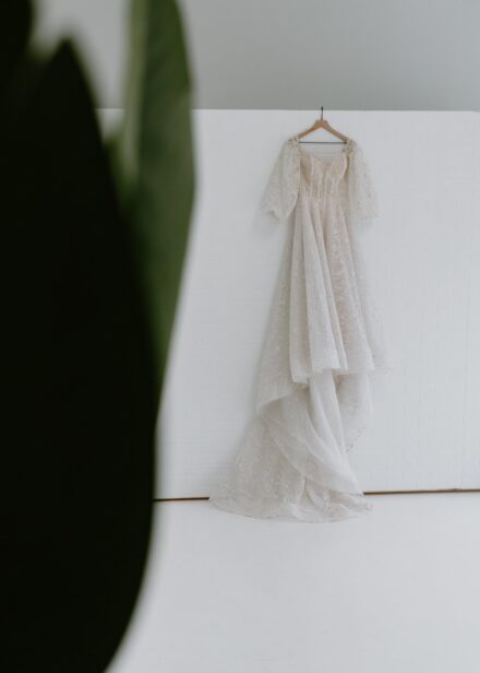 A wedding dress covered in glitter and stars hanging on a white wall.