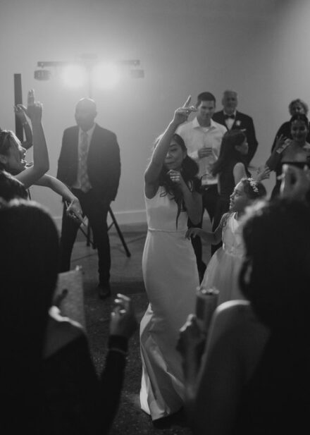 A black and white photo of the bride dancing with her wedding guests.