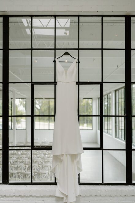 A minimal wedding dress hanging on a wall of windows at The Whim in Minneapolis.