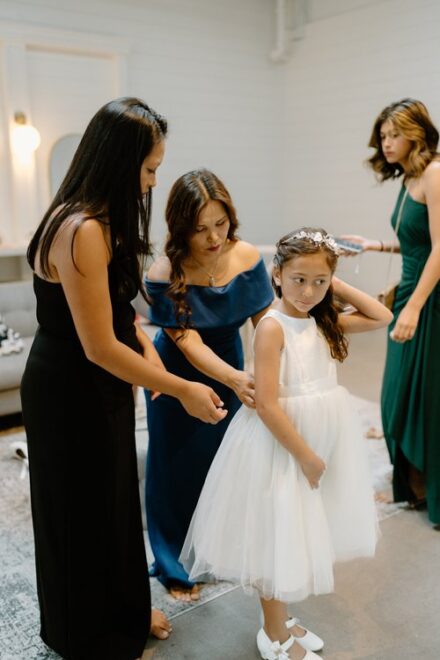Two family members zipping up a flower girl's dress.