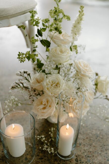 A white and green floral arrangement next to two lit white candles