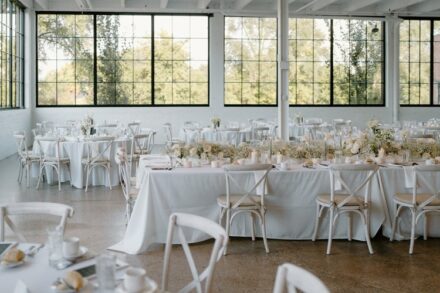 White chairs next to white tablecloth covered tables covered in white flowers.