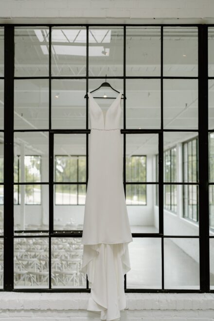 A minimal, white wedding dress hanging on a window at The Whim in Minneapolis