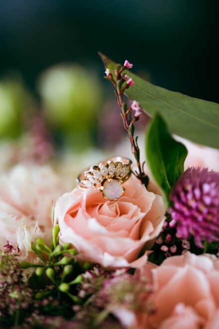 A rose gold wedding ring sitting on top of a baby pink rose in a flower bouquet.