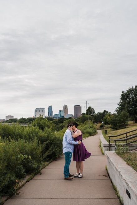 Abby and Jill kiss with the Minneapolis skyline in the background.