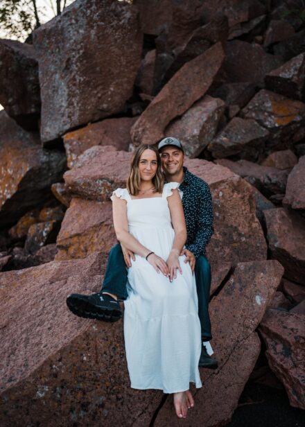 Taylor and Jesse sit on rocks below a cliff at Black Beach.