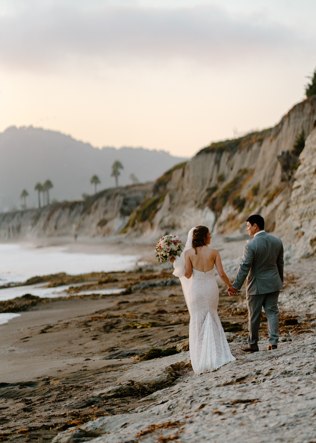 A wedding couple walking down the beach at sunset.
